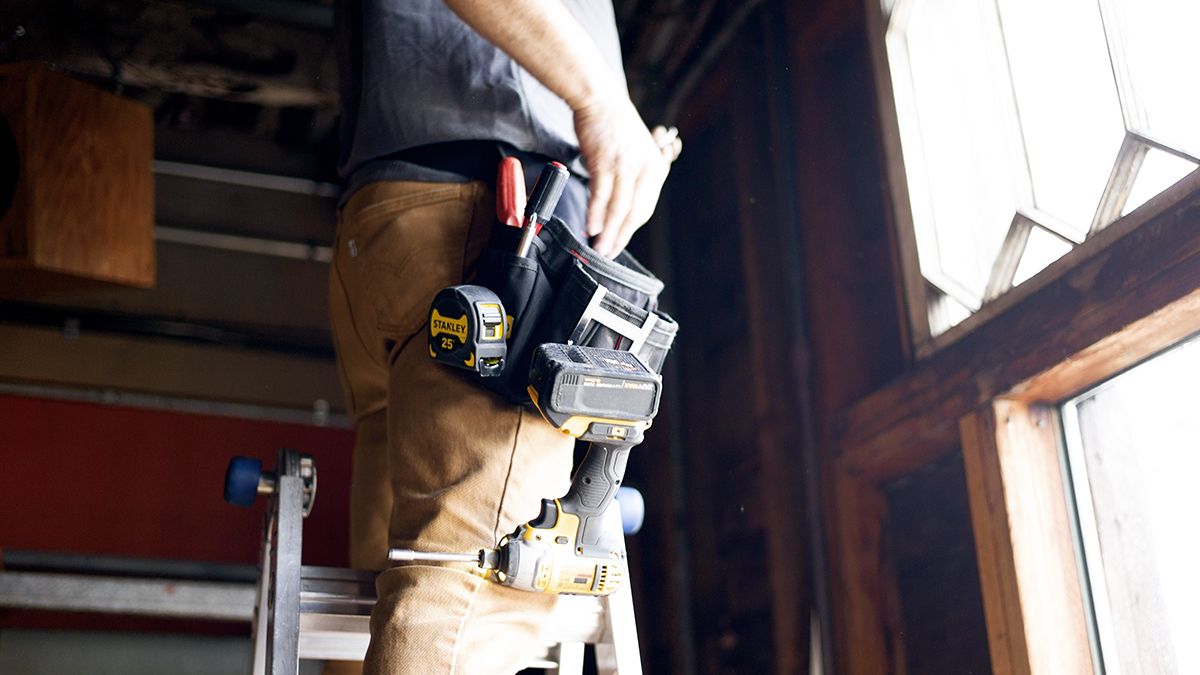 handyman standing on ladder with belt holding tools and electric drill