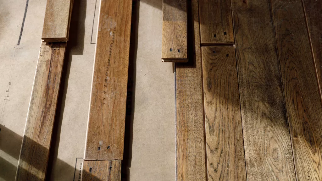 Pieces of hardwood flooring laying on brown paper partially installed.