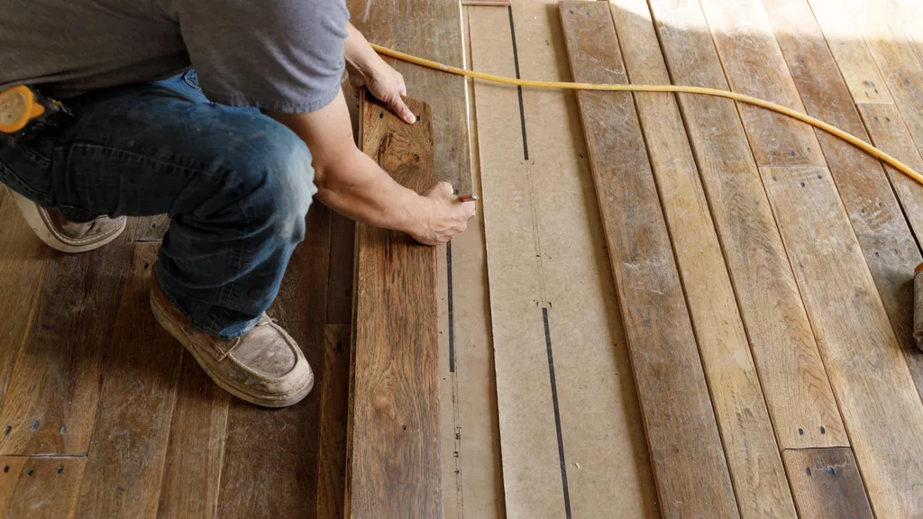 Person kneeling and marking wood to cut while installing a hardwood floor.
