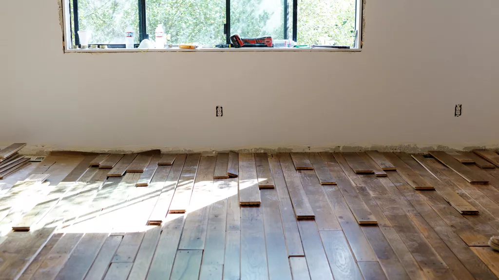 Hardwood flooring placed and waiting to be installed under a white wall with a window and tools on the sill.